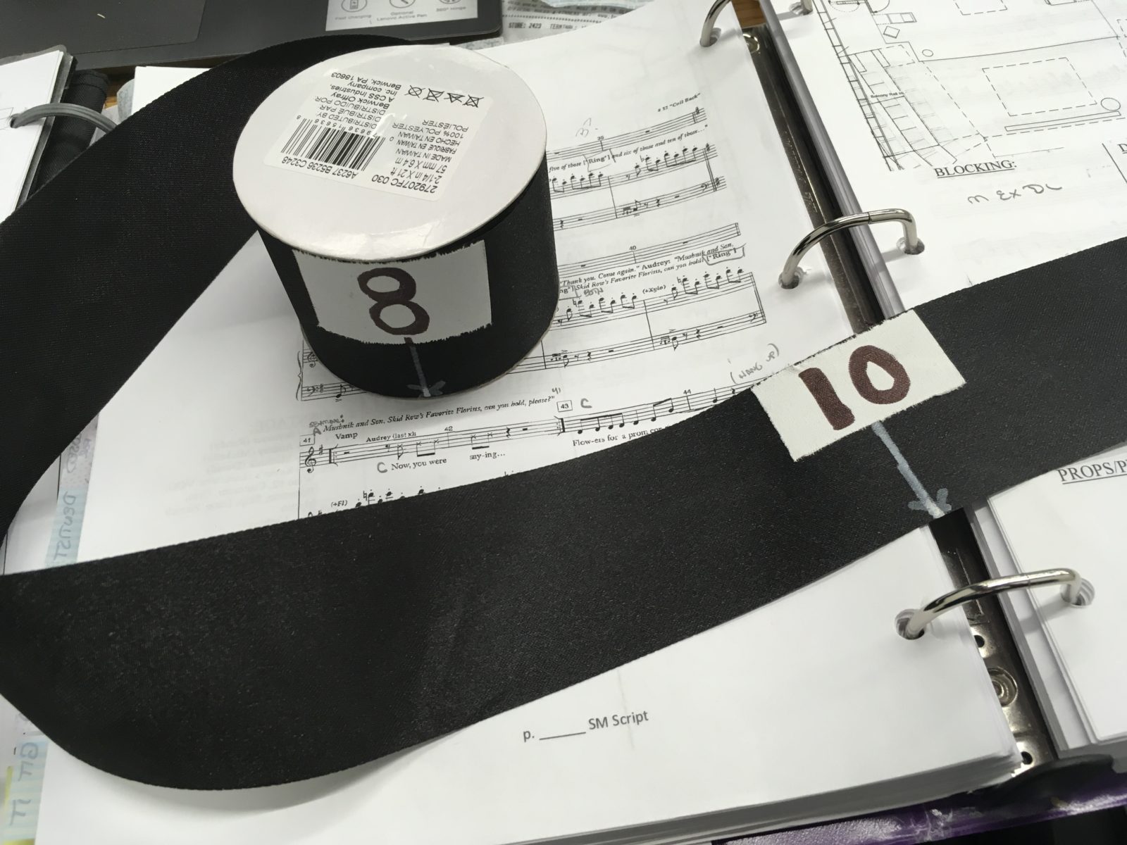 A portable dance number line made of ribbon sits on a stage manager's script