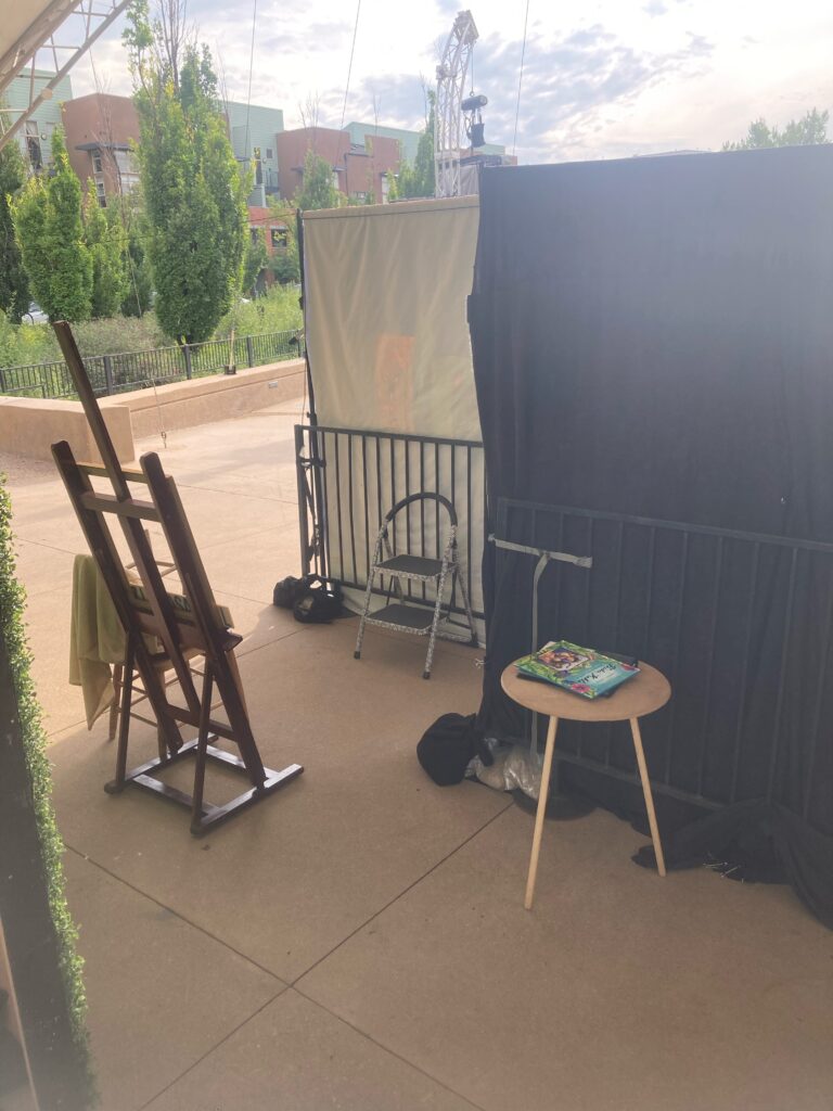 The view from backstage at an outdoor opera - pipe and drape drops are fastened to bike-rack style barricades for stability. Additional props and tables are preset behind them.