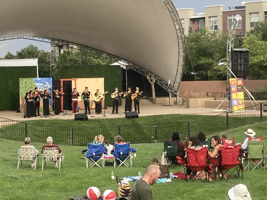 a Mariachi band performs outdoors in front of brightly painted scenic drops.