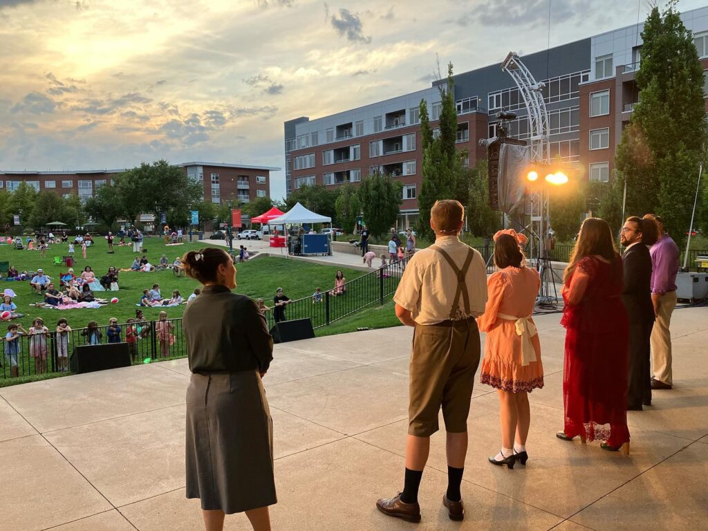 The view from behind singers during a question and answer section of an outdoor opera; the sun is beginning to set and the front row is filled with children hanging over the fence to be as close as possible to the performers.