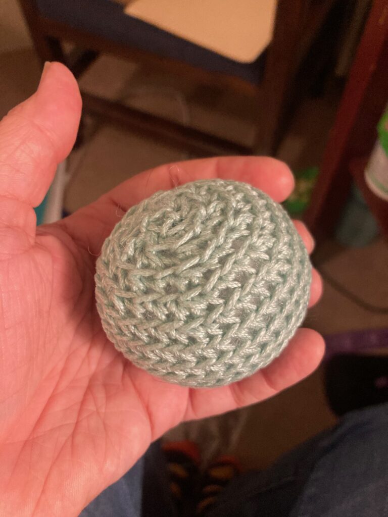 A hand holds a small round crocheted ball of green yarn