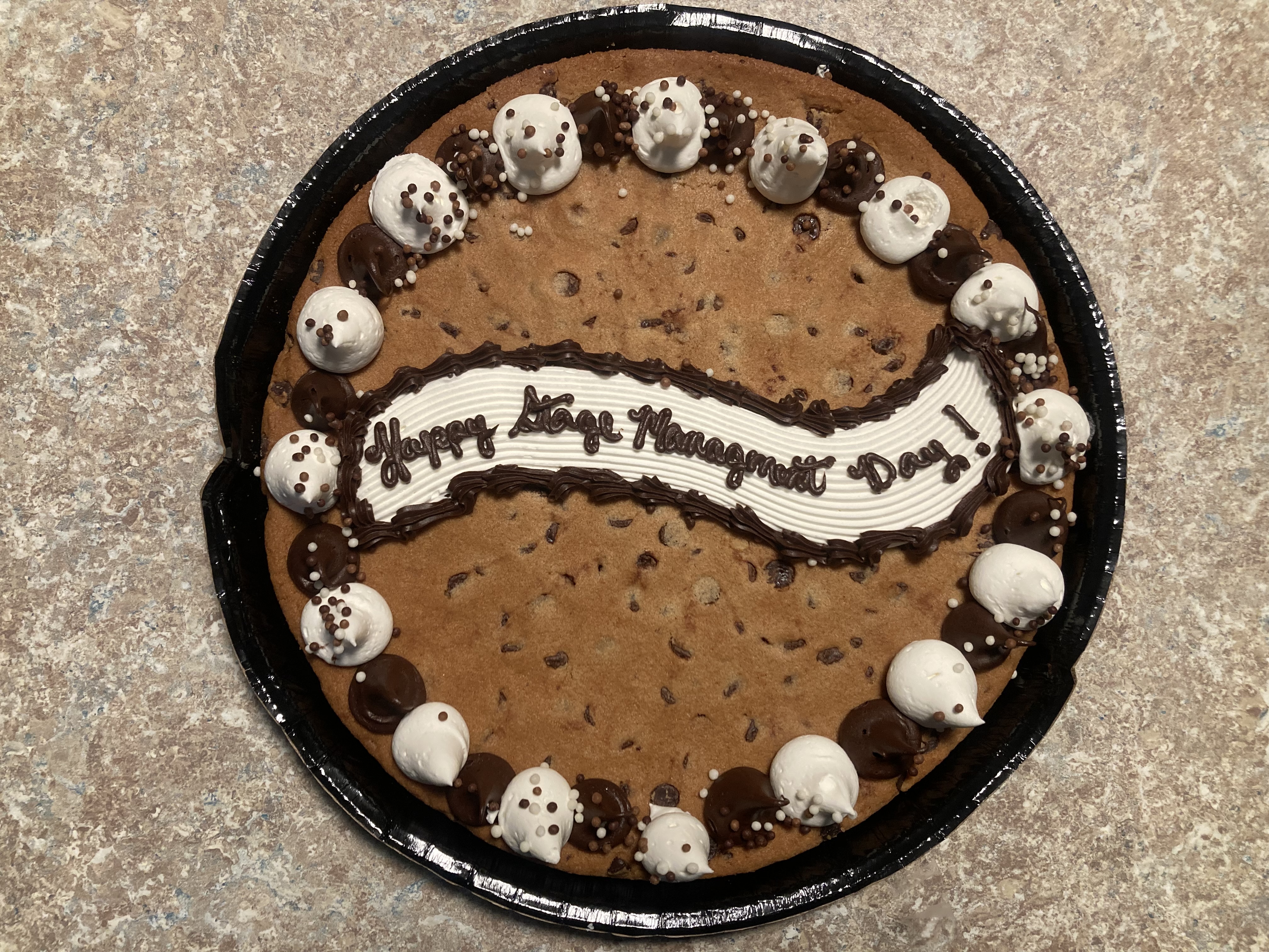 A chocolocate chip cookie cake has the words Happy Stage Management Day written in icing. Or maybe there is one less E in the words, hard to tell