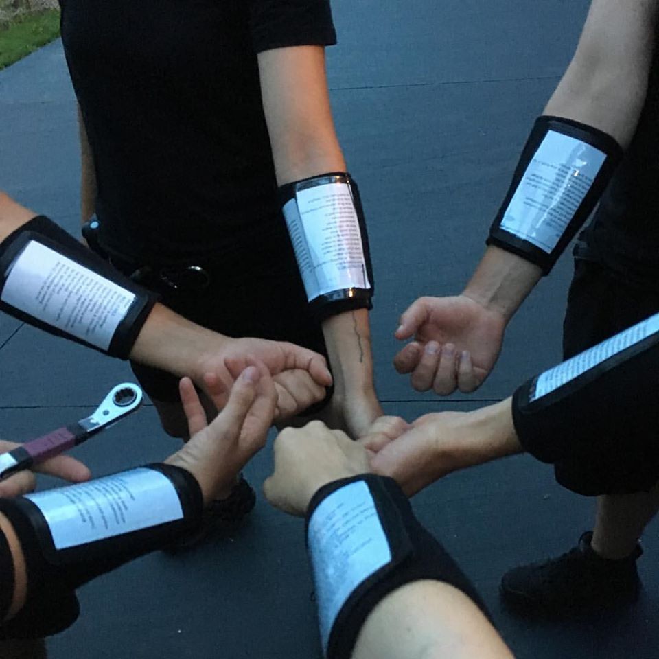 6 people have their arms in a circle, fists to center, showing off paperwork inside the type of sleeves used for quarterbacks