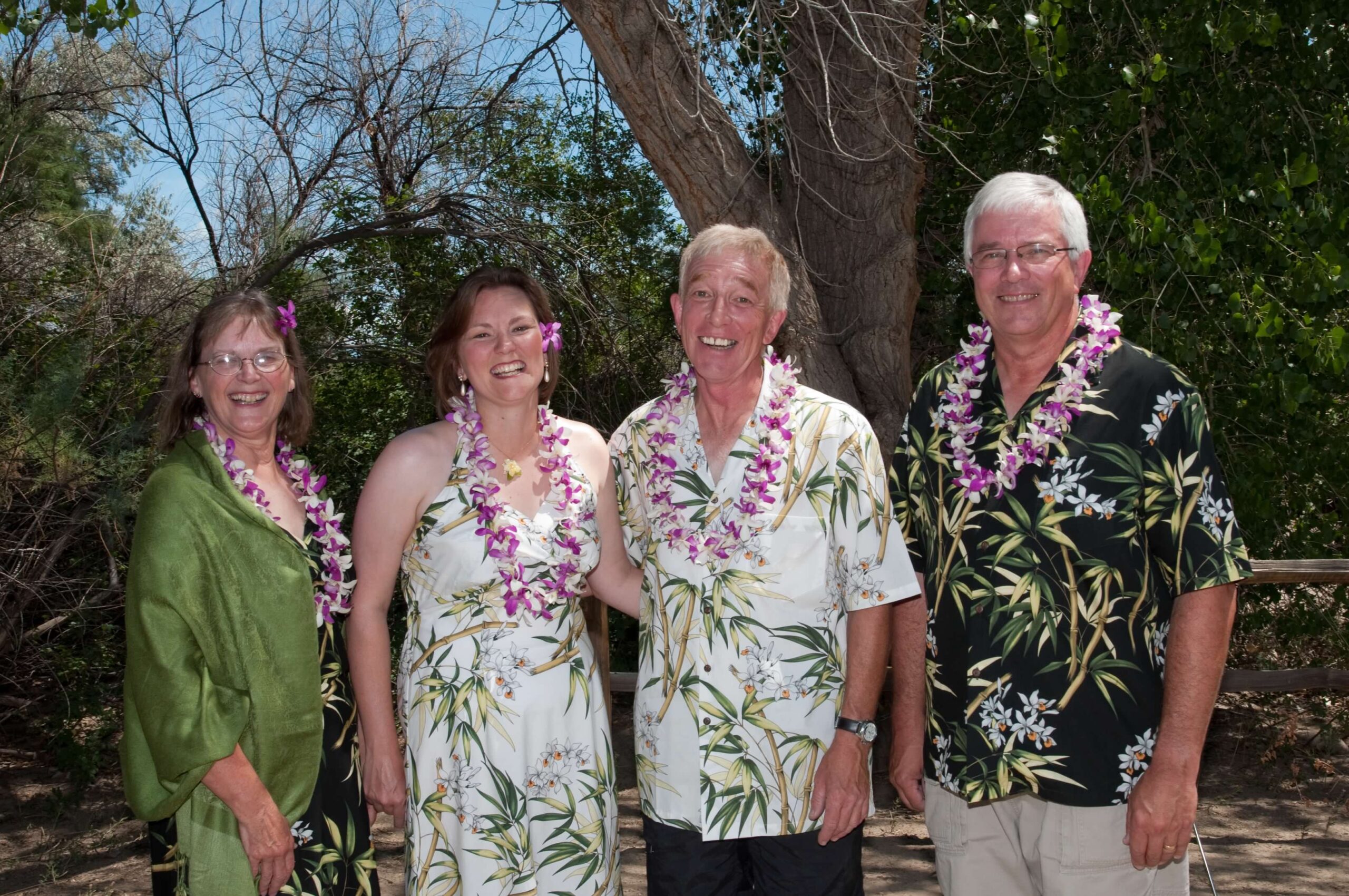 Four people in Hawaiian outfits, with Leis, smile at the camera.