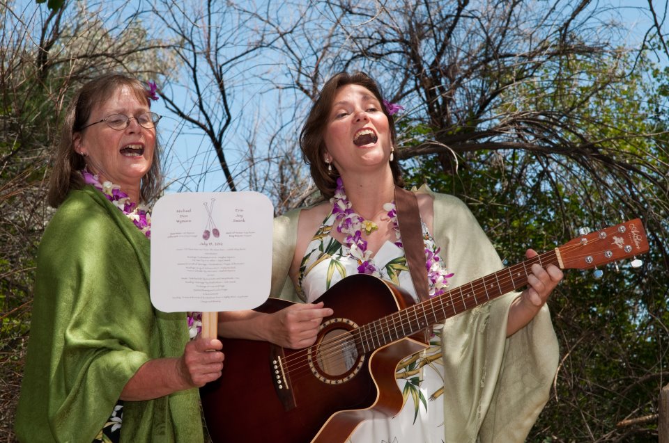 One woman holds a paper fan, another holds guitar and both are singing