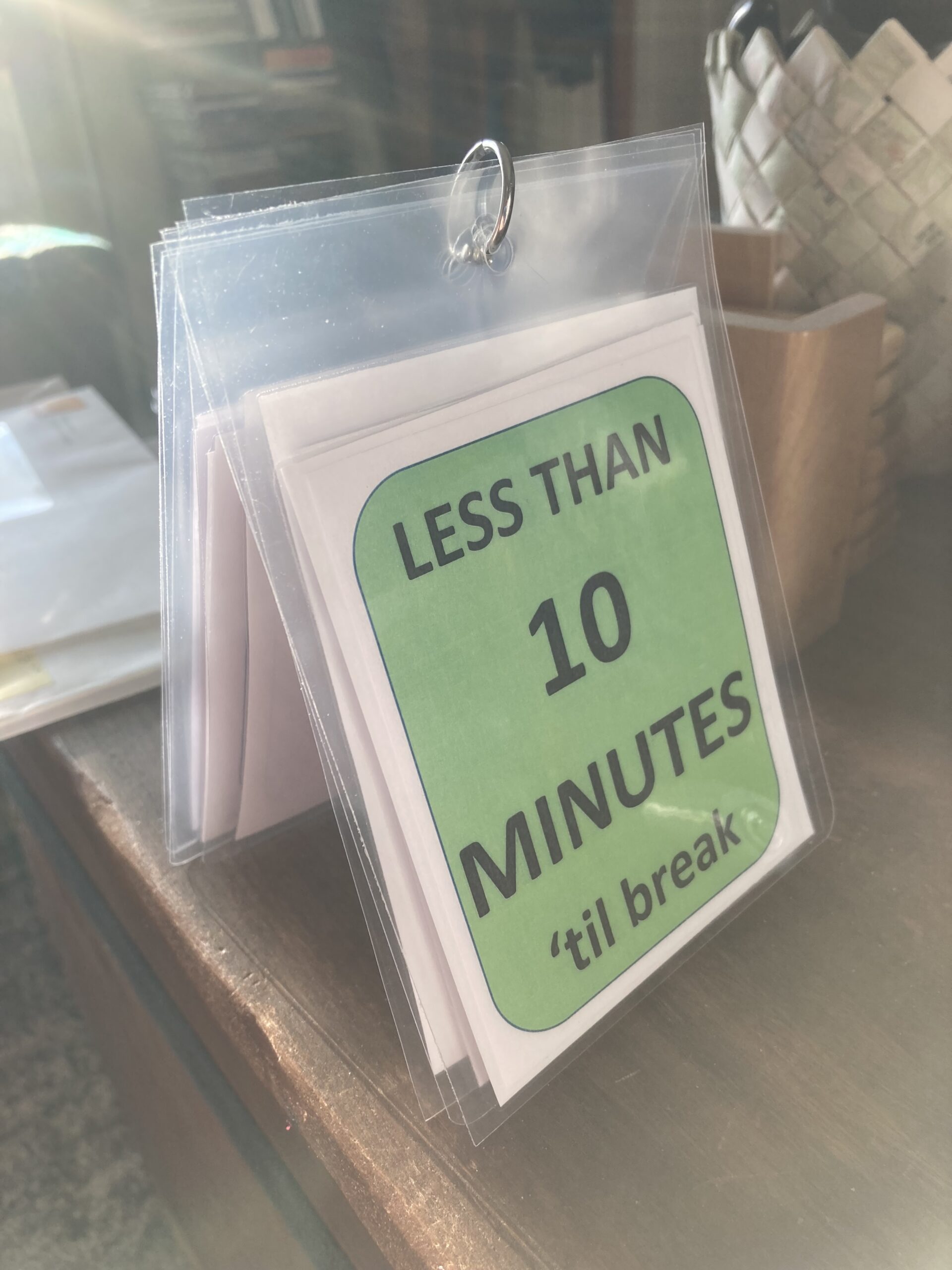 A laminated card reads less than 10 minute 'til break, on a green background. Multiple sheets are below it and they are connected by a small ring