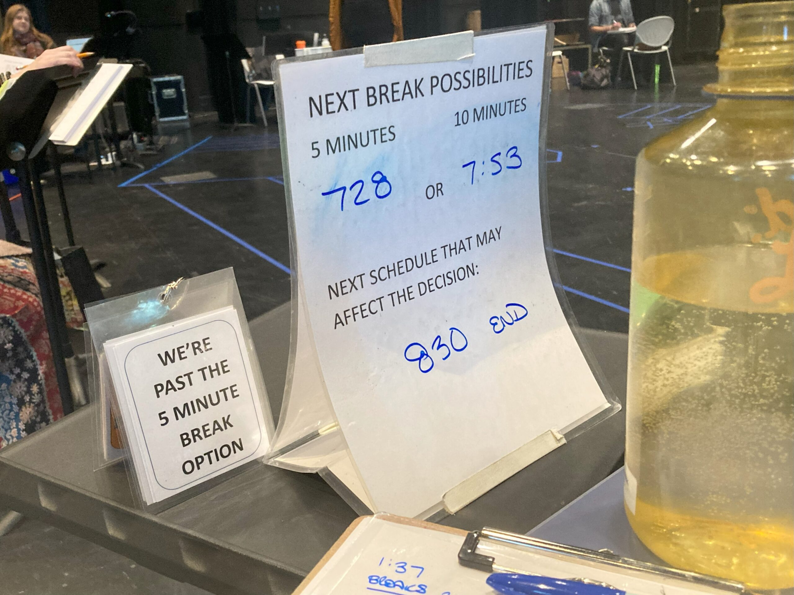 Laminated signs sit on a stage manager's table. One reads We're past the 5 minute break option, the other gives choices of what time to take the 5 and 10 minute breaks, and a notice that the end of the day is at 8:30p.