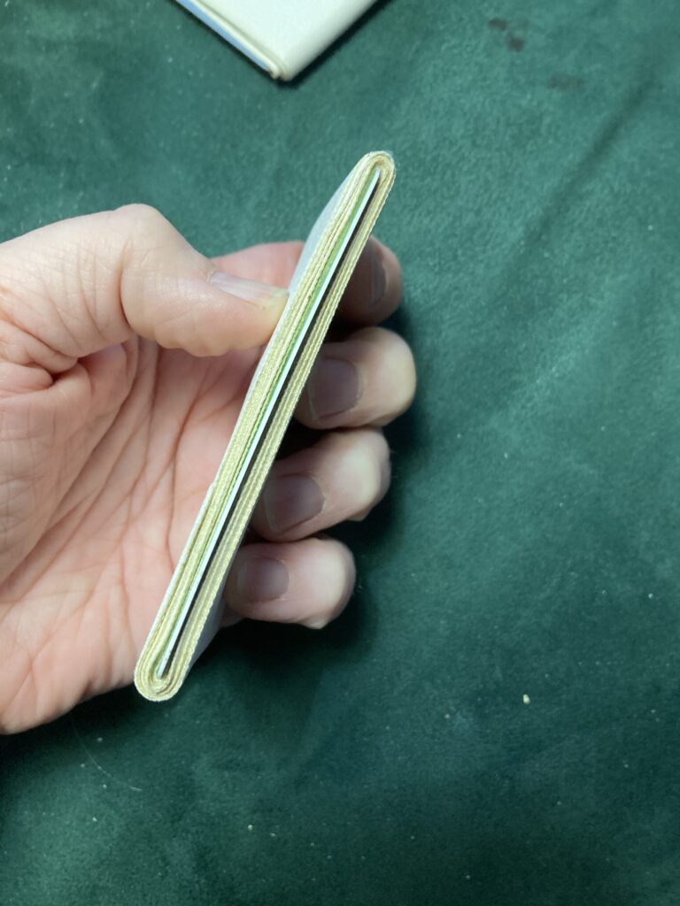 A hand holds a side view of white gaff tape wrapped around a plastic card, all on a green velvet background.